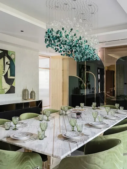 We designed this dining room as a central gathering place for celebration. The long marble dining table is surrounded by bespoke chairs upholstered in a rich green velvet, creating a sense of occasion. Overhead, a sculptural chandelier composed of green and clear glass pieces acts as a floating artwork, tying the entire space together.