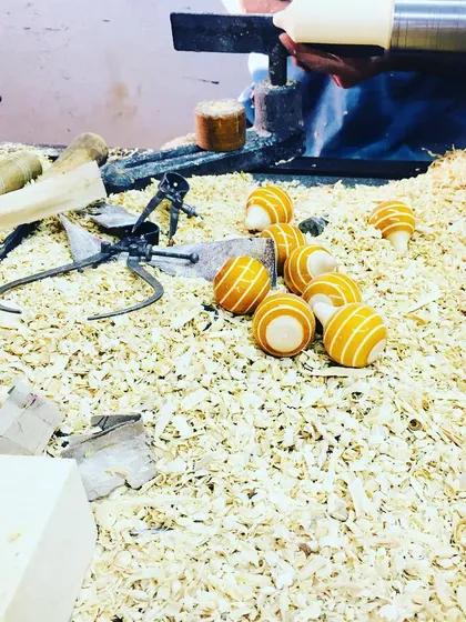 Freshly lacquered spinning tops rest in a bed of wood shavings. This image captures the vibrant colors and the raw, earthy environment of our factory floor, showing the toys at an intermediate stage of creation.