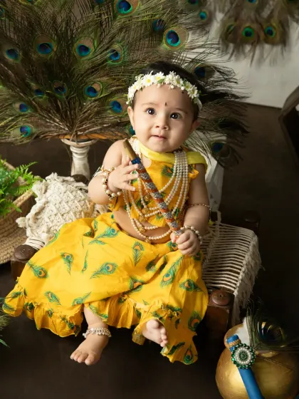 A beautiful portrait of a baby girl dressed in a yellow peacock-feather print outfit for Janmashtami.
