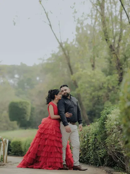 A classic portrait from an engagement shoot in a lush Pune garden. The woman's striking red gown and the couple's confident pose create a timeless and elegant image, showcasing a more formal and styled approach to pre-wedding photography.