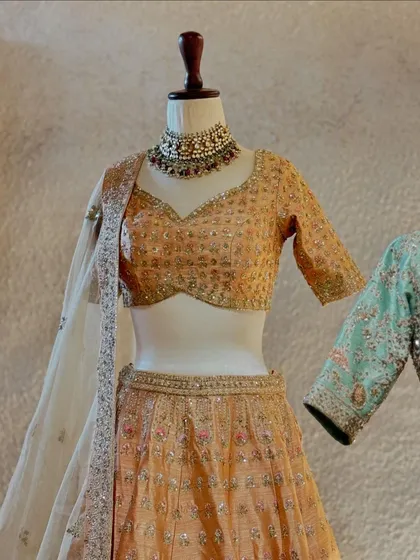A detailed shot of the peach lehenga, focusing on the sweetheart neckline and the intricate sequin and threadwork on the blouse.