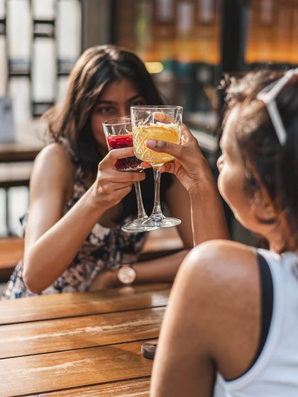 Two friends sharing a toast with colorful drinks at our Indiranagar outlet, a perfect spot to wine and dine.
