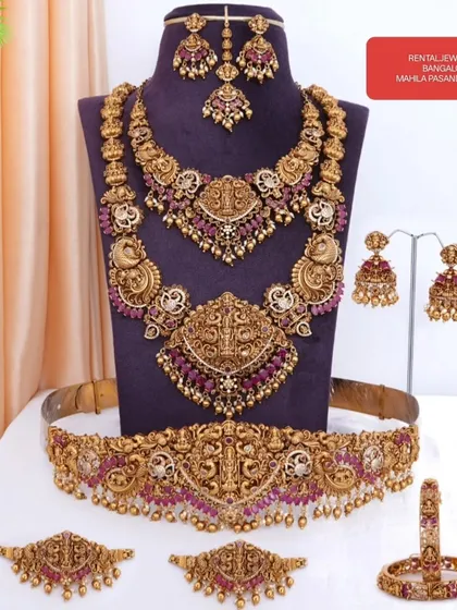 Here is a full bridal set laid out so you can see every beautiful piece. This ruby-studded temple jewellery set includes a choker, haram, vaddanam (waist belt), vanki (armlets), jhumkas, and a maang tikka. Everything you need for a complete bridal look is right here.