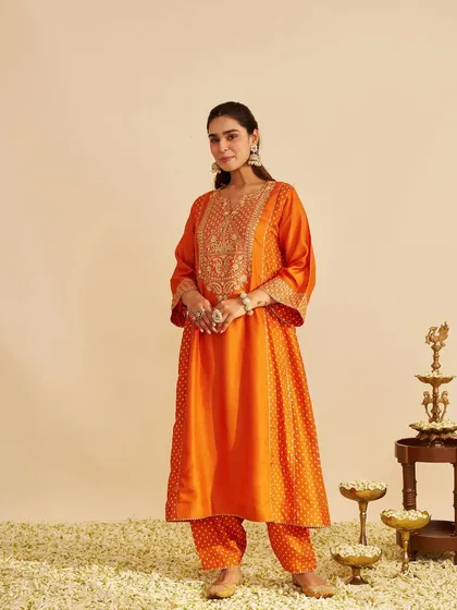 This vibrant orange kurta set is perfect for any festive occasion. The model is surrounded by flowers, enhancing the celebratory feel of the outfit.