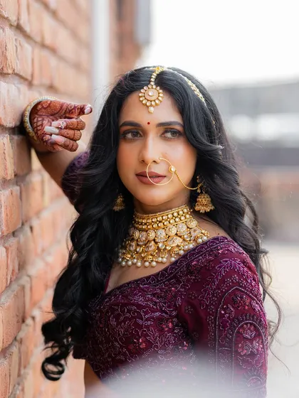 A stunning portrait of the bride against a brick wall. Her traditional jewelry and elegant pose create a timeless and beautiful image.