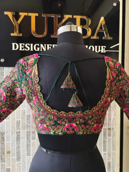 A full view of the back of the emerald green blouse, showing the deep U-neck and custom tassels. The dense embroidery covers the entire surface, making it a true statement piece.
