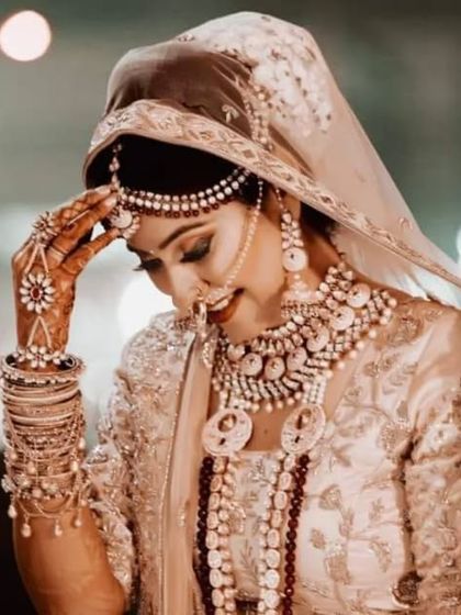 A candid and beautiful bridal portrait. The bride is looking down with a shy smile, a classic pose that captures the modesty and grace of a traditional Indian bride.