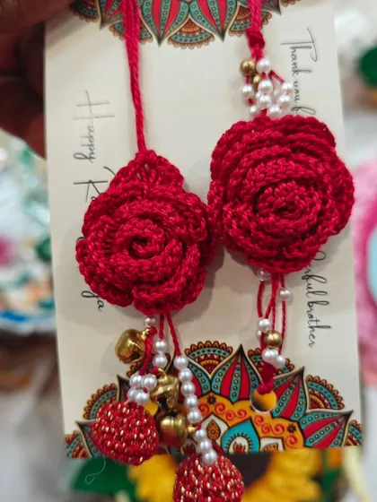 A detailed look at the red rose lumba rakhi, complete with hanging crochet balls, pearls, and festive bells.