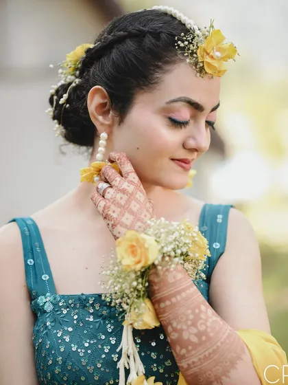 A beautiful close-up of the bride during her Haldi, showcasing her floral jewelry and the intricate henna on her hand.