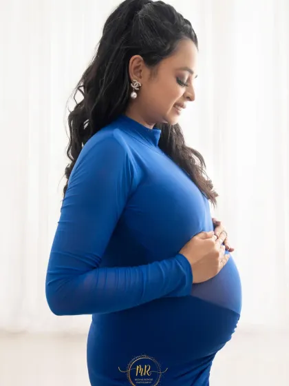 A close-up profile shot capturing the mother's serene expression. She is wearing a modern royal blue dress, gently holding her baby bump.