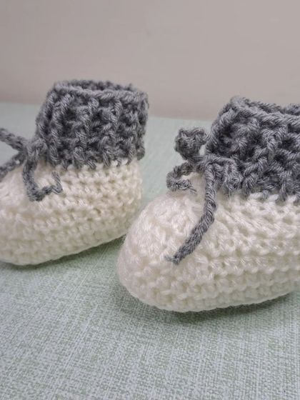 These unisex baby booties in grey and white are a modern and versatile choice, with a fold-over cuff and tie closure.