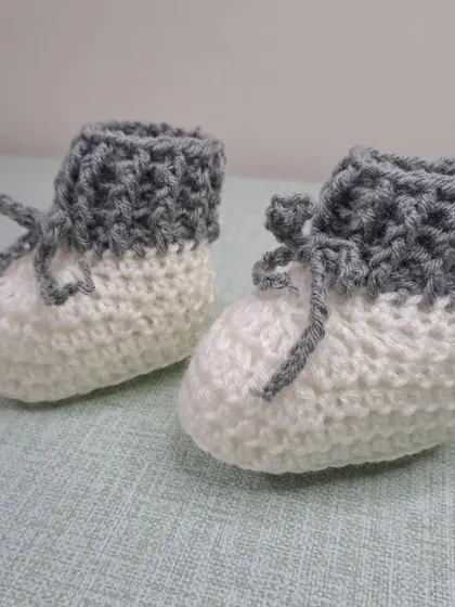 These unisex baby booties in grey and white are a modern and versatile choice, with a fold-over cuff and tie closure.