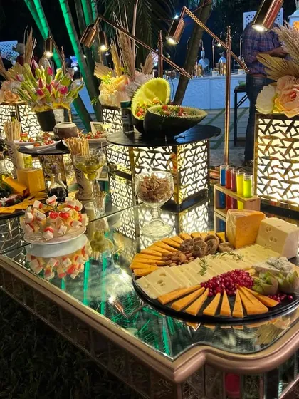 A magnificent mirrored table displaying a full cheese station. The spread includes multiple cheese platters, fruit displays, and other gourmet bites, creating a luxurious focal point.