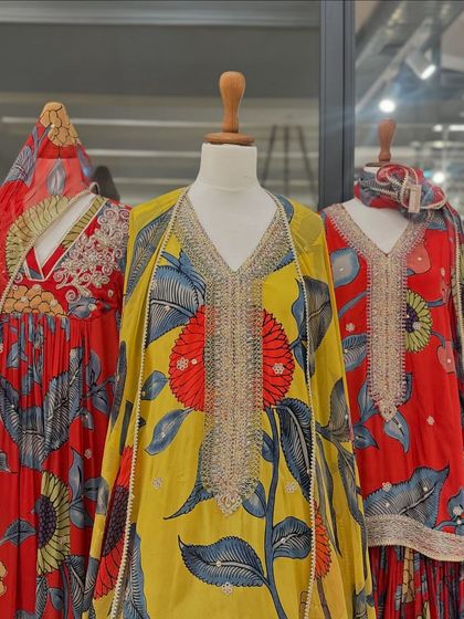 A vibrant display of festive floral printed outfits in shades of red and yellow, featuring heavy silver embroidery around the necklines.