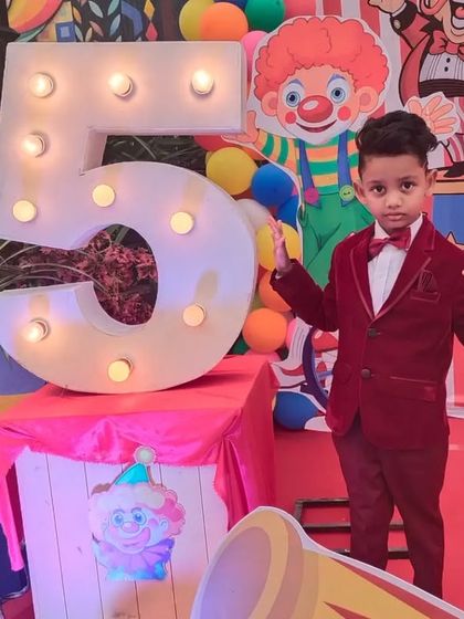 The birthday boy, dressed for the occasion, poses next to a giant light-up number '5' at his amazing carnival party.