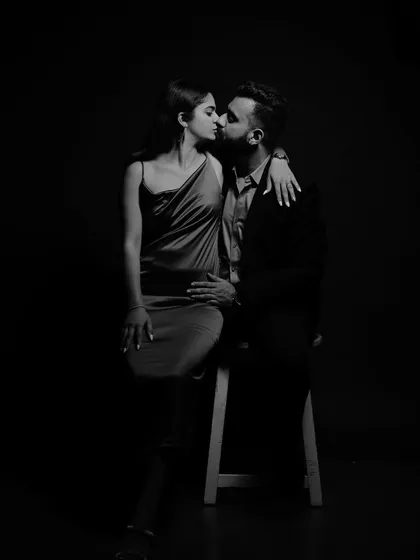 A romantic and elegant black and white portrait of the couple sharing a kiss. The low-key lighting creates a dramatic and intimate atmosphere.