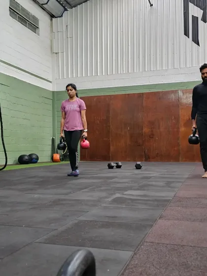 Members performing a dual kettlebell farmer's carry during a group workout. This fundamental movement translates directly to real-world strength, like carrying heavy groceries with ease.