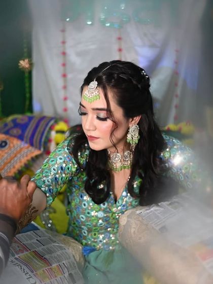 A candid moment during the mehendi application. The bride's makeup is soft and pretty, with a mint green maang tikka matching her outfit.
