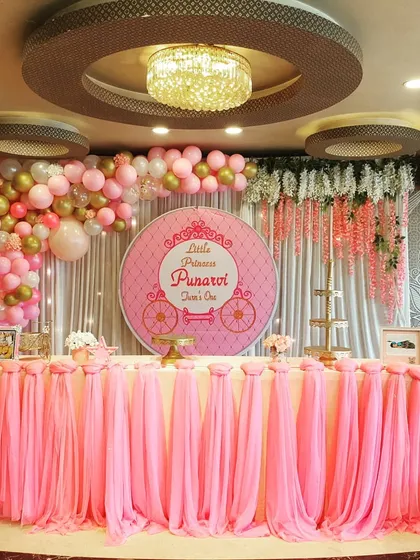 A classic princess theme brought to life for Punarvi's first birthday. The main stage features a grand cake table with elegant pink draping, set against a custom circular backdrop and a full balloon arch in pink, white, and gold chrome.