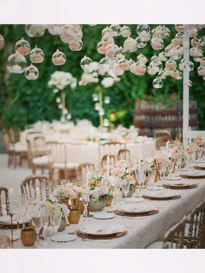 A breathtaking sit-down dinner setup with a ceiling of hanging glass orbs filled with pink roses. The attention to detail in the floral arrangements and place settings creates a truly high-end feel.