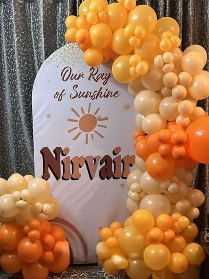 A warm and cheerful "Our Ray of Sunshine" themed decoration. This simple yet beautiful setup uses an arched backdrop and a balloon garland in shades of orange, yellow, and cream, perfect for a naming ceremony or first birthday.