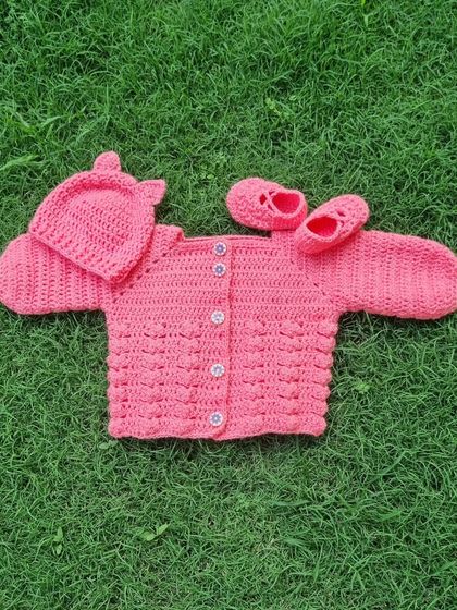 This complete three-piece baby set in a lovely coral pink is ready for a new home. It includes a textured bubble-stitch sweater, little slip-on booties, and a matching hat with cute bear ears.
