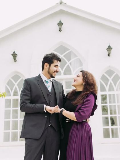 A formal portrait of the couple in front of the white chapel. Their coordinated outfits and happy expressions make for a timeless pre-wedding photograph.