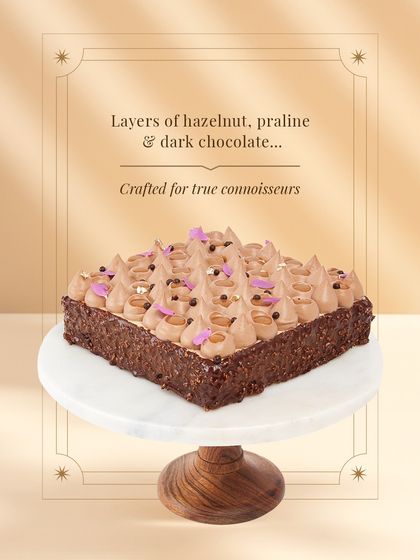 The Go Nuts For Hazelnuts entremet, presented on a marble stand. This square creation is layered with hazelnut, praline, and dark chocolate, crafted for those who appreciate an intense and rich dessert experience.