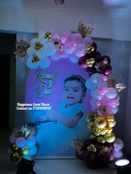 A premium U-shaped balloon decoration for a first birthday. This design uses a custom photo backdrop and a sophisticated color palette of maroon, pink, white, and gold balloons.