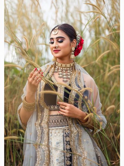 An outdoor bridal shoot capturing a serene and elegant moment. The natural setting complements the traditional lehenga, and the soft lighting highlights the delicate details of the fabric and embroidery.