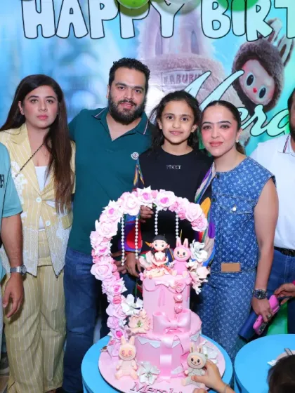 A family gathers for a cake-cutting ceremony at a Labubu-themed birthday party. The intricate cake and themed backdrop make the moment extra special.