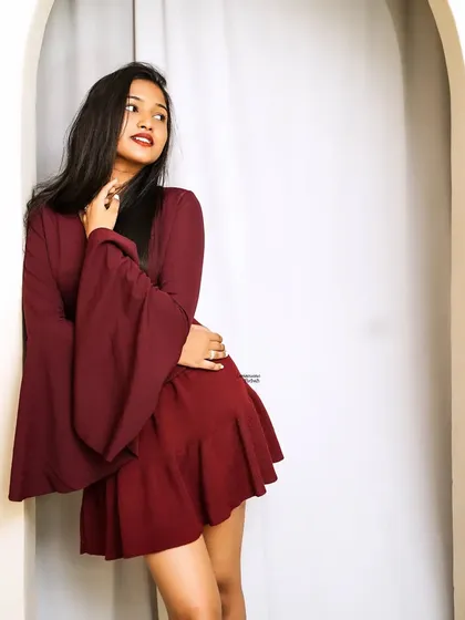 A thoughtful and serene pose, with the model looking away, framed by a white archway that contrasts with her deep red outfit.