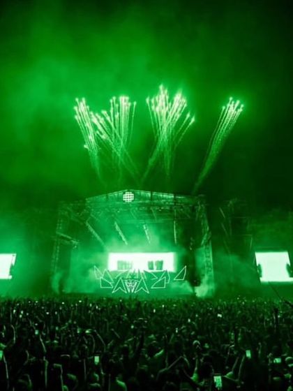 The entire stage and crowd are bathed in an intense green light, punctuated by fireworks, during the Alan Walker concert.