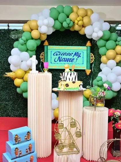 A naming ceremony setup with a green foliage wall and a balloon ring. The "Guess My Name" sign is a central feature, and I used decorative pedestals for the cake and other items, creating a complete stage for the event.