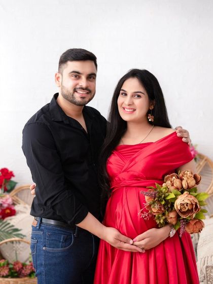 A classic couple's portrait in our romantic floral setup. The husband stands behind his wife, his hands gently on her bump, as they both smile for the camera.