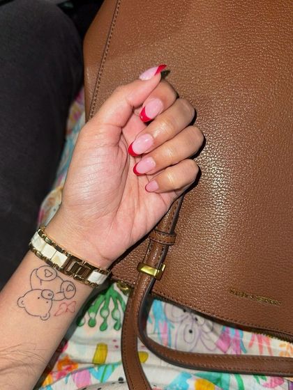 The final look of these vibrant red French tips, perfectly matching a chic brown leather bag.