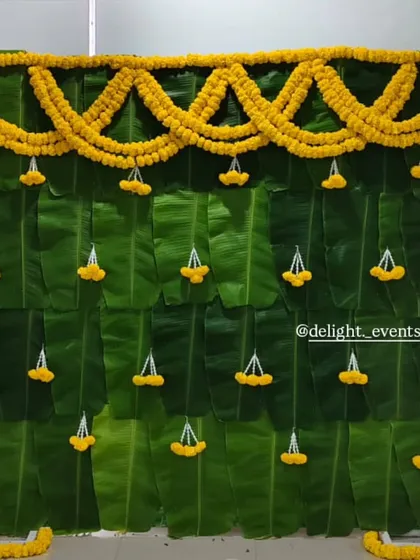 For an authentic and natural touch, we design beautiful backdrops like this one made entirely of fresh banana leaves. The simple marigold garlands and jasmine tassels make it perfect for home functions like a baby shower or pooja.