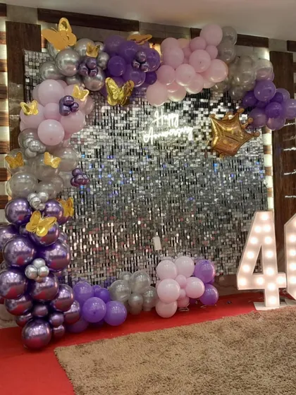 Celebrating milestones like a 40th anniversary deserves something special. I put together this elegant photo booth with a silver shimmer wall, a balloon arch in purple and silver, butterfly accents, and large marquee numbers.