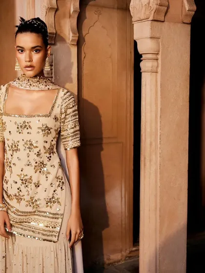 A full-length view of a model wearing a stunning beige sharara set, showcasing its graceful fall and the shimmer of the sequin work.