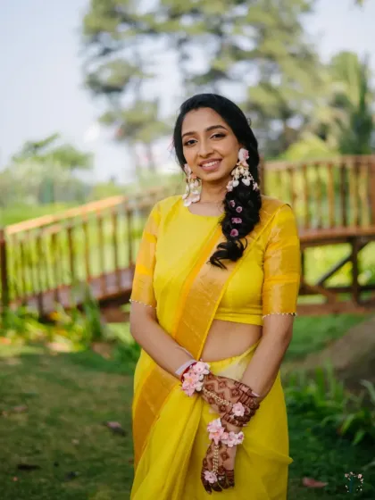 A smiling portrait of the bride in her vibrant yellow saree for the Haldi ceremony, adorned with delicate floral jewellery.