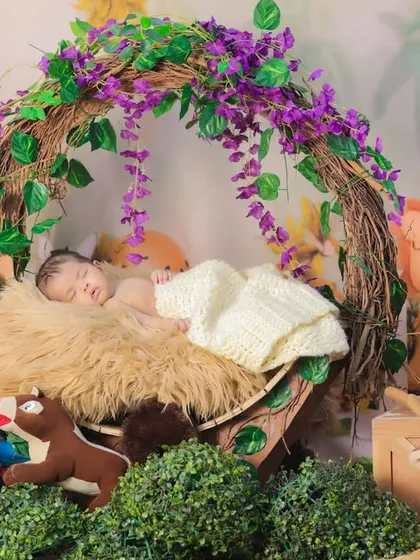 A newborn sleeping in a basket decorated with a vine arch, surrounded by jungle animal toys. This creates a safe and cozy jungle nook for the baby.