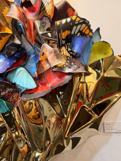 A close-up of "Wings of Resilience." This view shows the layering of the polycarbonate wings and the way they are integrated with the crumpled, reflective gold stainless steel base.