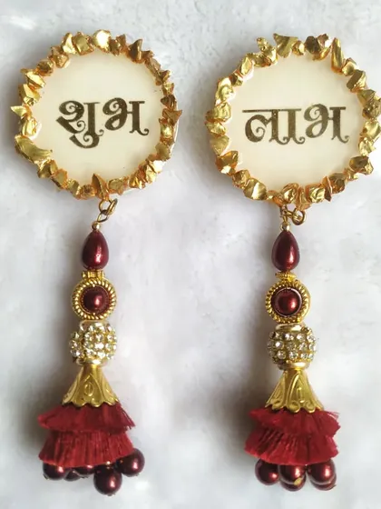 These 'Shubh Laabh' door or wall hangings are perfect for inviting good fortune into your home during festivals. This design features elegant script on a white resin base with a decorative red tassel.
