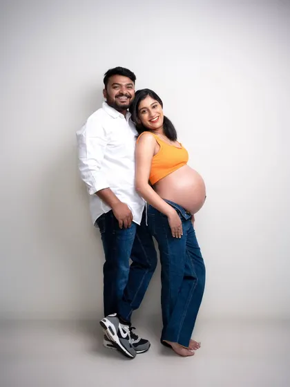Casual, confident, and glowing with happiness. The pop of orange against the simple white background adds a burst of energy to this modern maternity portrait. Their relaxed pose shows their comfort with each other.