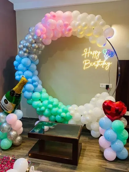 A multi-colored pastel balloon ring with a neon sign and champagne bottle prop.