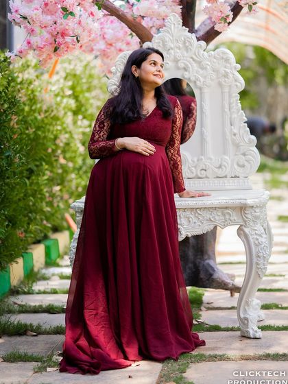 A graceful solo maternity portrait. The mother-to-be looks up thoughtfully, standing by an ornate prop, creating a moment of quiet reflection during the family shoot.