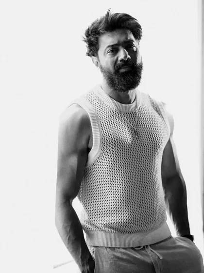 A high-key black and white portrait of Dev Adhikari. The bright background and his strong, direct gaze create a clean yet powerful image that focuses entirely on his presence.