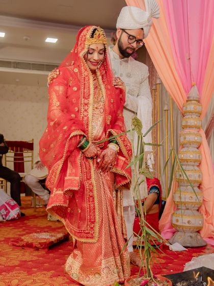 A candid moment from the wedding ceremony. The bride and groom are seen performing rituals, and her traditional red outfit looks beautiful in the warm light.