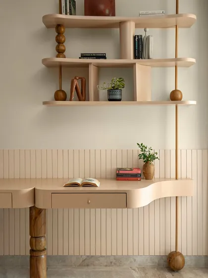 This study nook, part of a master bedroom, features a custom-designed desk and shelving unit with soft, organic curves and turned-wood details. The design is light, airy, and feels deeply personal.