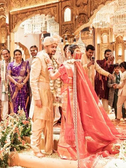 The couple during the varmala ceremony, surrounded by a garden of flowers on the stage. The rich colors and textures create a beautiful, timeless moment.